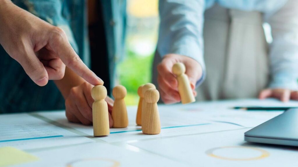 Immagine di un team che collabora con dei segnalini in legno su di un tavolo per sottolineare il consiglio strategico per sfidare la complessità